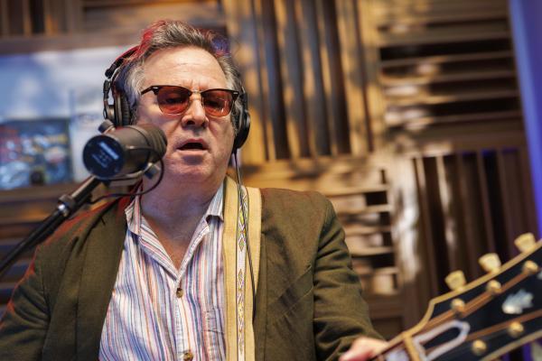 LOWER TIGHT PHOTO OF GRANT LEE PHILLIPS IN FRONT OF MICROPHONE PLAYING GUITAR